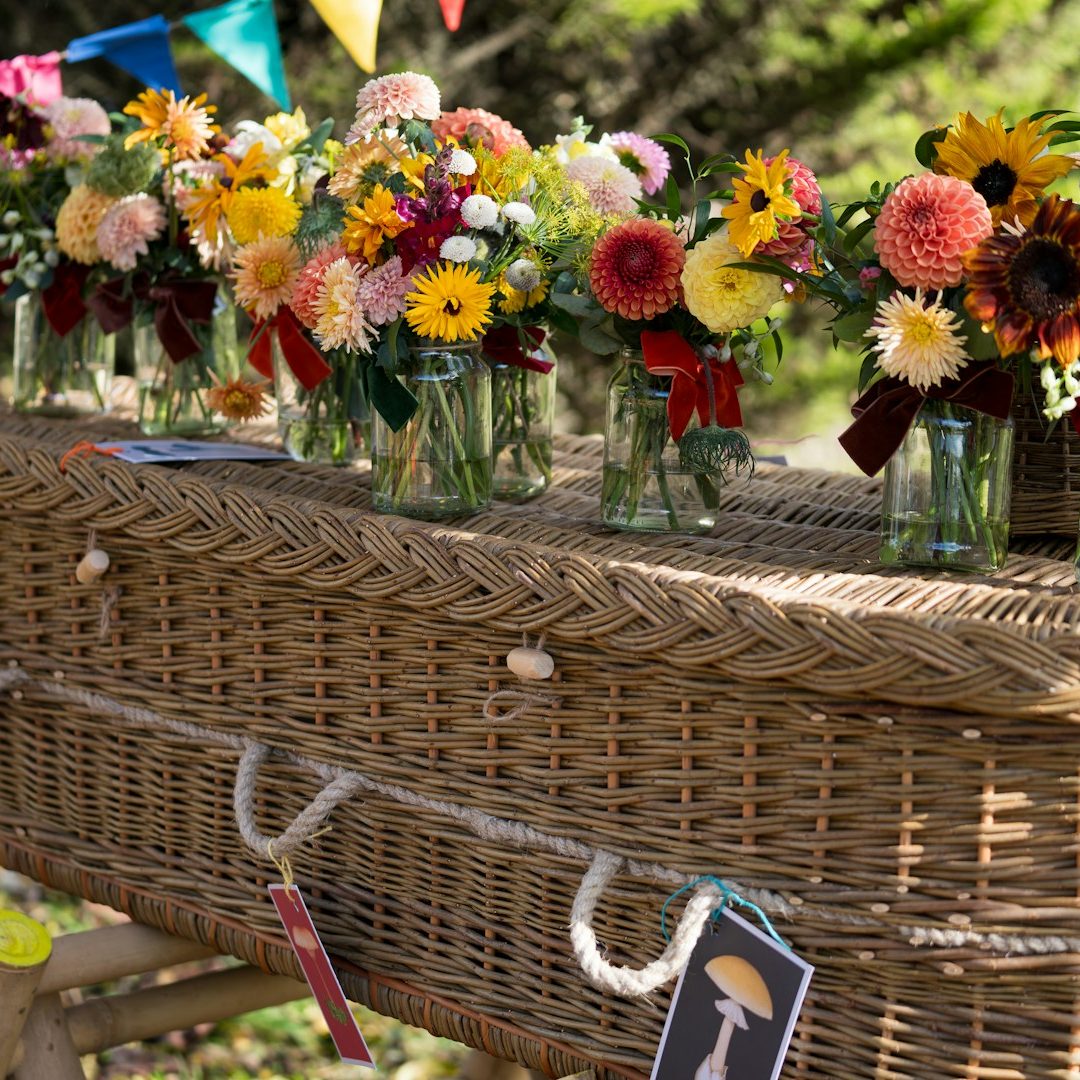Wicker coffin decorated with beautiful flower jars Wicker coffin decorated with flowers for a simple cremations on the Isle of Wight by Life Funerals